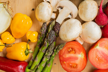 wooden board with vegetables. mushrooms, tomatoes, asparagus, broccoli, peas, peppers and basil
