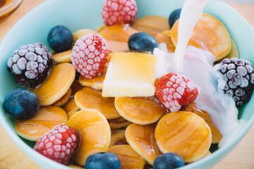 Close up bowl full of cereal pancakes with raspberries, blueberries, and blackberries with syrup and milk poured in