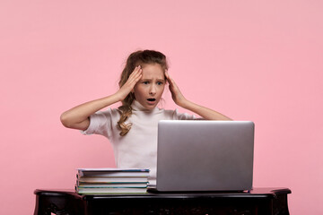 A young girl in a white shirt looks frightened at the monitor screen