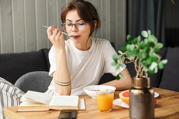 Photo of beautiful focused woman reading book while having breakfast