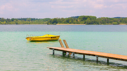 Wooden pier leading towards a yellow boat. Landscape at lake Wörthsee, Bavaria / Germany.