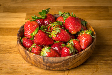 cuenco de madera lleno de fresas con sus tallos verdes
