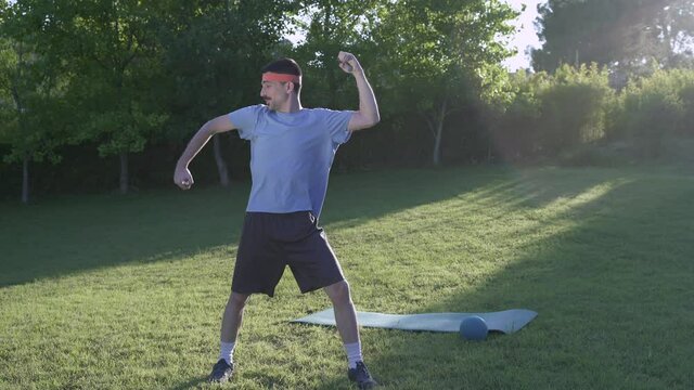 Funny retro man doing sport isolated on a park. Flexing muscle and stretching before workout. 80's Sport guy training in garden. Fun train in the grass.