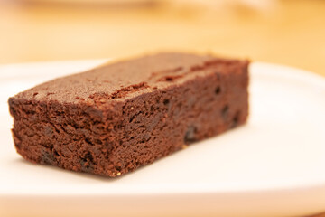 Delicious dark chocolate brownie on white plate with warm lighting at bakery shop. 