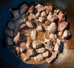 The meat is fried in oil on a cast-iron cauldron.