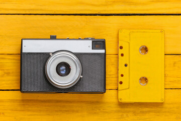 Retro audio cassette and film camera on a yellow wooden background. 80s. Top view