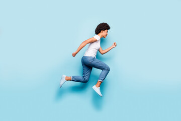Full size photo of beautiful dark skin curly lady jumping high rushing marathon finish line coming first active sporty person wear casual white t-shirt jeans isolated blue color background