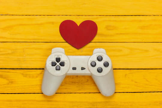 Game lover. Retro gamepad with red heart on yellow wooden background. Retro 80s. Top view.