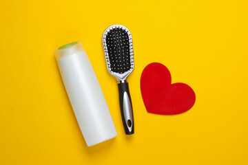 Shampoo bottle, hairbrush with heart on yellow background. Beauty and hair care. Top view. Flat lay. Minimalism