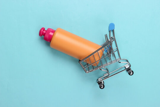 Mini supermarket trolley with shampoo bottle on blue background. Top view
