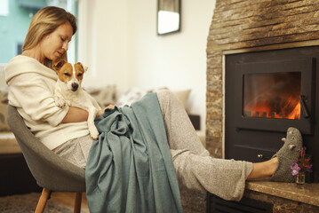 Cozy mountain weekend, Woman in cozy home wear relaxing near fireplace, hugging dog