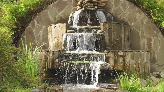 Decorative waterfall with rocks and plants in the Park. Beautiful place with an artificial waterfall in the Park.