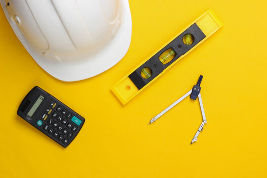 Hard hat with building level, calculator, compass on yellow studio background. Engineering, construction equipment. Top view