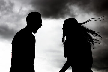 Silhouettes of arguing couple against sky with heavy rainy clouds. Relationship problems
