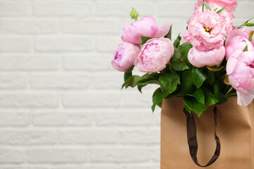 The concept of flowers, floristry, holiday. Pink peonies in a craft bag, against the background of a white brick wall. Mock up. Copy space.