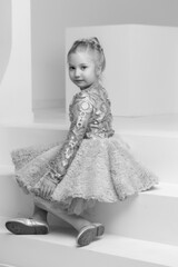Cute little girl is sitting in the studio on the white stairs. style and fashion concept, happy childhood.