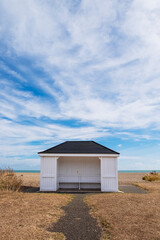 White wooden beach shelter on Aldeburgh Beach, with wispy cloudscape. Aldeburgh, Suffolk UK.
