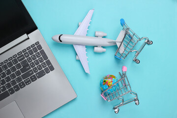 Air delivery. Global supermarket. Online shopping. Shopping trolley with globe, laptop, airplane figurine on blue background. Top view. Flat lay