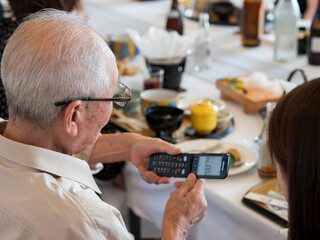 An elderly Asian man struggling to use an old fashioned flip phone