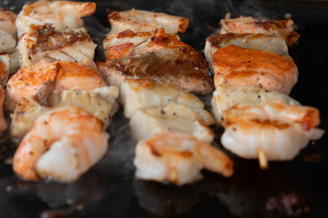 Shrimps and salmon cooking on black barbecue background