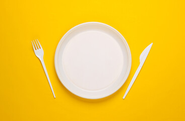 Plastic plate with fork and knife on a yellow background. Picnic. Plastic pollution. Top view