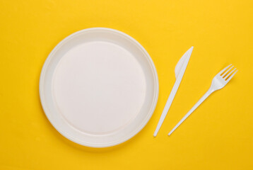Plastic plate with fork and knife on a yellow background. Picnic. Plastic pollution. Top view