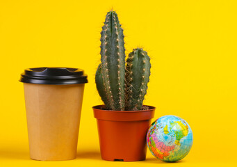 Cactus in pot and coffee cup, globe on a yellow studio background. Minimalism
