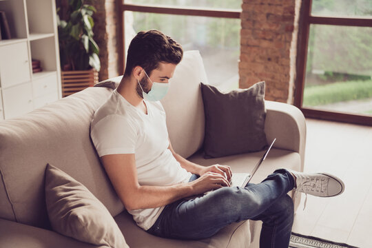 Profile photo of student young guy chatting notebook freelance job internet coach typing keyboard sms message quarantine stay home wear facial medical mask sit couch living room indoors