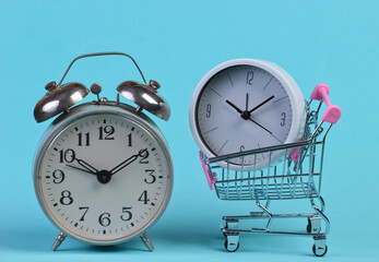 Shopping time. Supermarket trolley with alarm clocks on blue background