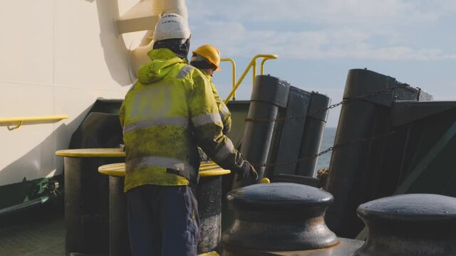 industrial Natig Aliev tanker deck crew in special reflective vests and protective helmets casts moorings off close view
