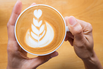 Hands holding a cup of latte top view wooden background.Latte art coffee top view.