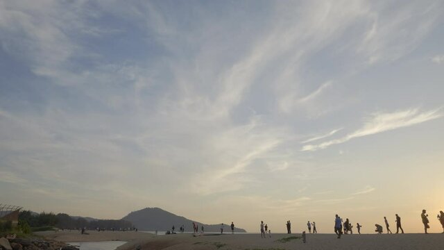 A panorama of people are walking and taking photos in sunset beach near airport with beautiful blue sky and hills in background