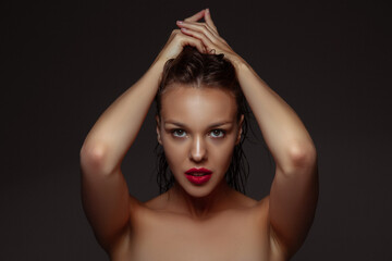 Fototapeta premium Natural purity. Portrait of beautiful stylish woman isolated on dark studio background. Caucasian model with red lipstick, wet hair and shiny skin, bright make up. Beauty, fashion, emotions concept.
