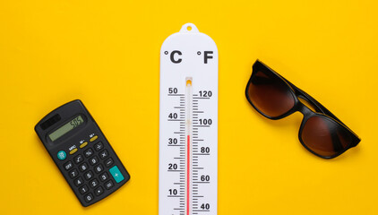 Global warming concept. Climate control. Weather thermometer and calculator, sunglasses on yellow background. Summertime. Top view.