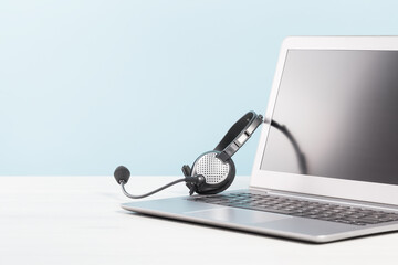 Laptop with blank screen with headphones. white desk blue background. copy space. Distant learning or working from home, online courses or shopping minimal concept. Helpdesk or call center headset - obrazy, fototapety, plakaty