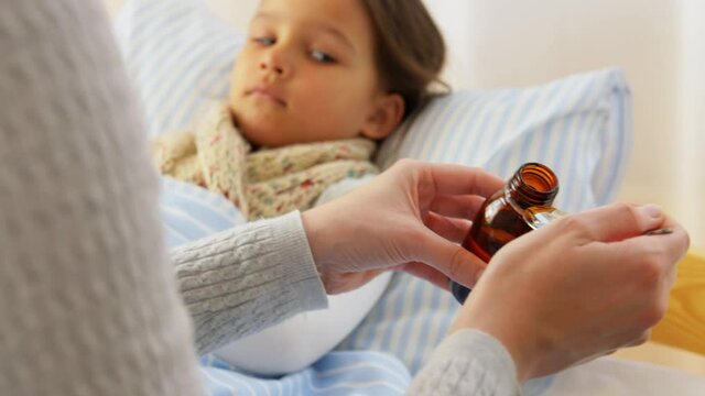 family, health and people concept - mother's hands pouring cough syrup for sick daughter lying in bed at home