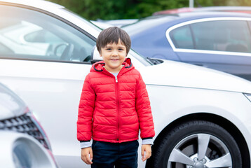 Kid standing next to the cars at the carpark, Child boy wearing red hoodie standing alone looking...