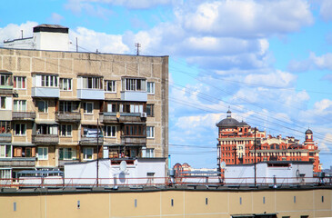 Satellite dishes and power line wires on metal roof of residential building against background of other multistory residential panel buildings and blue sky. A lot of wires on roof of house