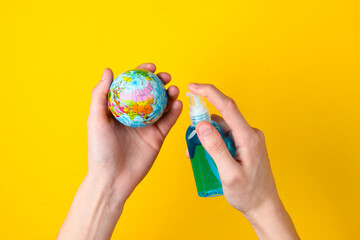 Hands holding a globe and disinfected with an antiseptic on a yellow background. Pandemic covid-19