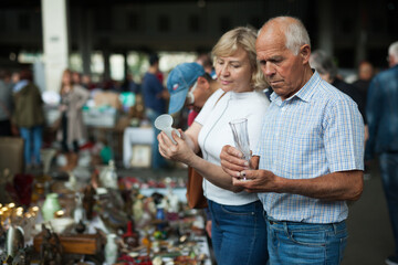 Attentive mature spouses buying retro handicrafts on flea market
