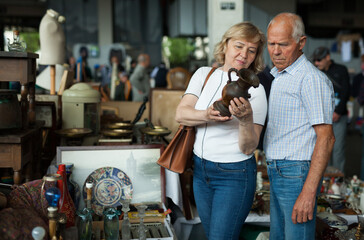Fototapeta na wymiar Smiling mature spouses buying retro handicrafts on flea market
