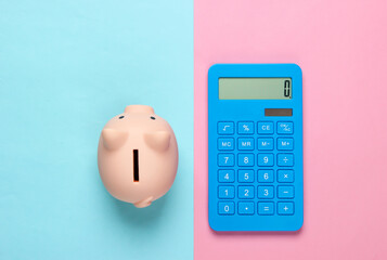Piggy bank and blue calculator on pink blue pastel background. Minimalistic studio shot. Overhead view. Flat lay.