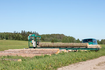 Mobile sawing equipment for logs and a work minibus in the open air. Rural landscape on a sunny day