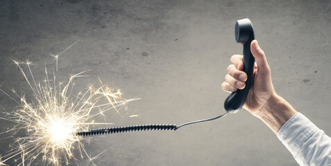 Businessman holds a telephone handset with a burning telephone cord