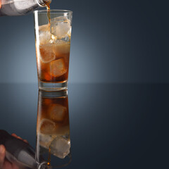 The ice cubes are clear in the glass and pouring the Coca Cola bubbles in a tall glass with reflections on a dark background.