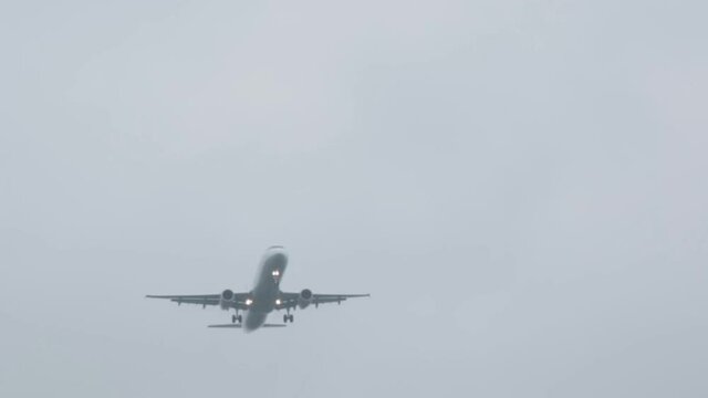 Plane flying over camera. Wide to close shot. Cloudy day with fog.