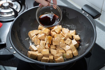 Cooking diced cubed dried tofu on gas stove in home kitchen, lifestyle, closeup.