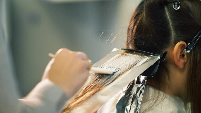 Professional Hair Stylist applying a creamy hair dye with a tint brush. Hair colouring with hair foil sheets. 