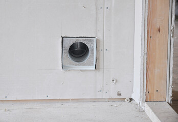 Installing an internally fitted round air vent and duct in a drywall near the door entrance during house renovation.