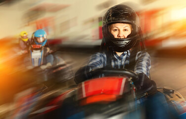 Fototapeta na wymiar Girl and her friends competing on racing cars at kart circuit